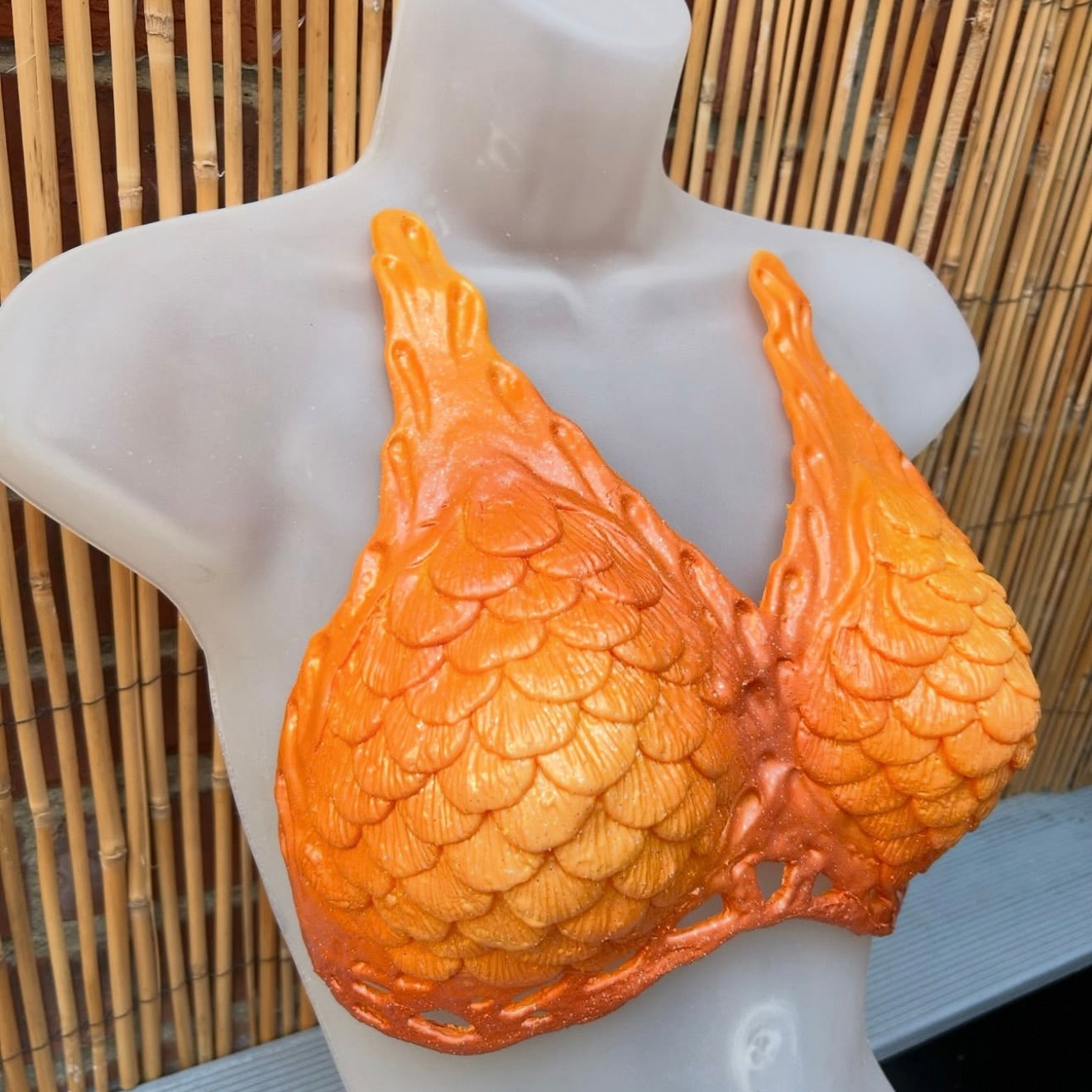 Orange Custom Mako mermaid top in silicone with skin-tone power mesh, swimmable and sleek design.  Textured bra on a mannequin.
