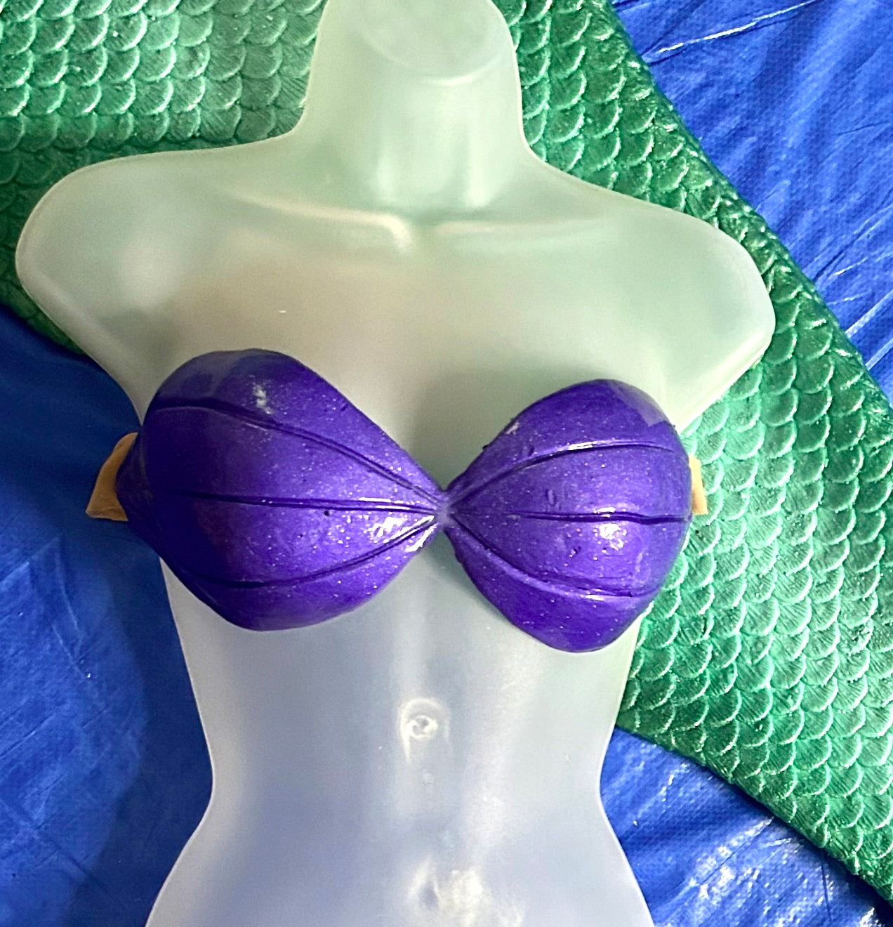Purple bikini top on a mannequin against a blue and green textured background. Disney little mermaid Ariel mermaid top shell bra swimmable