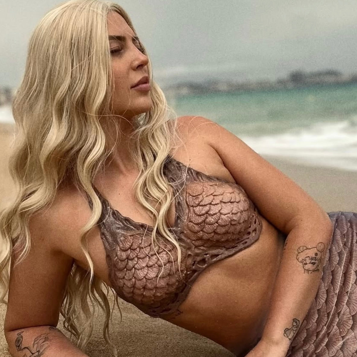 Swimmable silicone Mako mermaid bra for cosplay and underwater photoshoots. Mermaid in a silicone top sitting on a beach with ocean in the background. brown bra