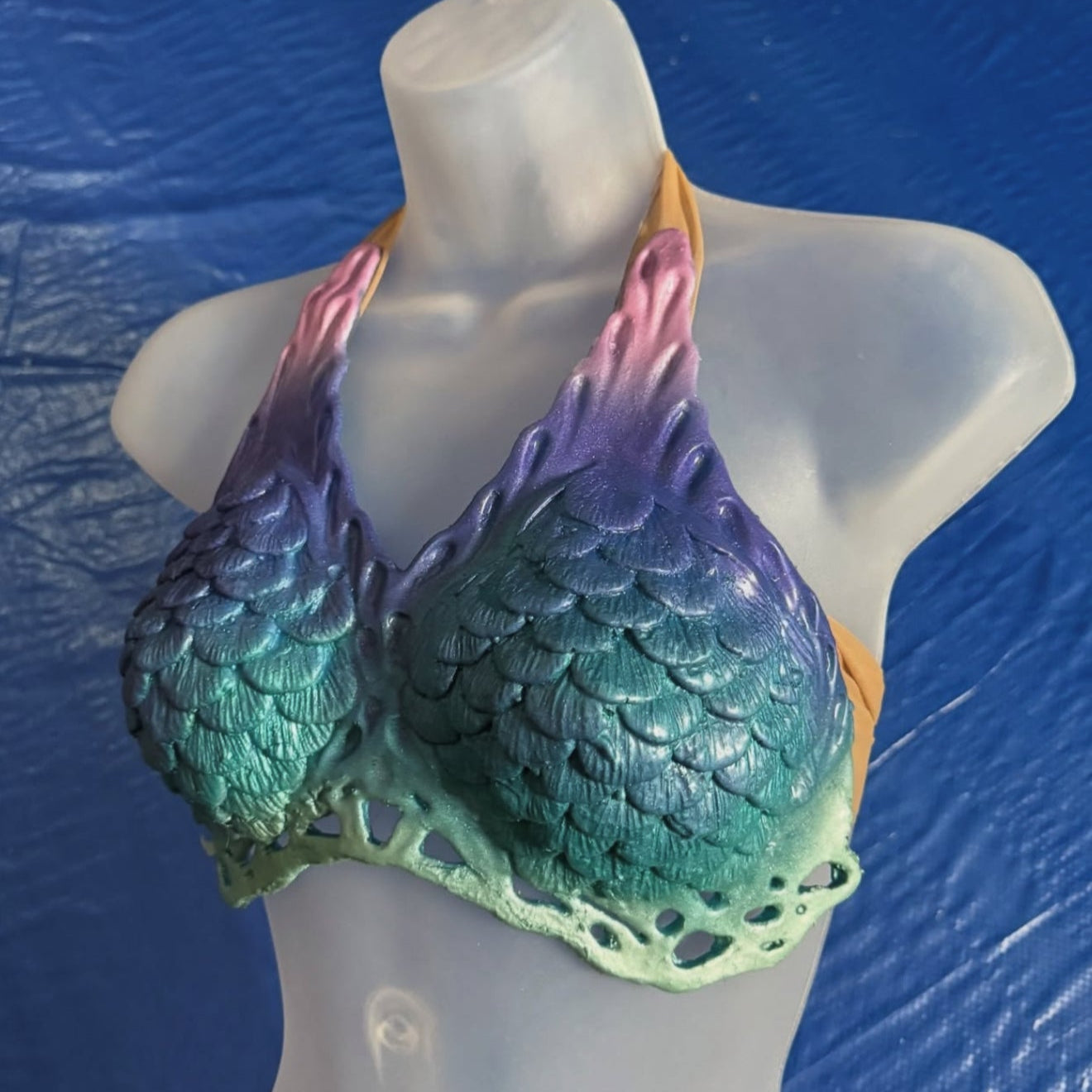Colorful fish-scale patterned top on a mannequin against a blue background. Mako mermaid top design rainbow colors